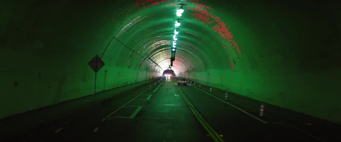 Cars drive through a tunnel and down city streets at night