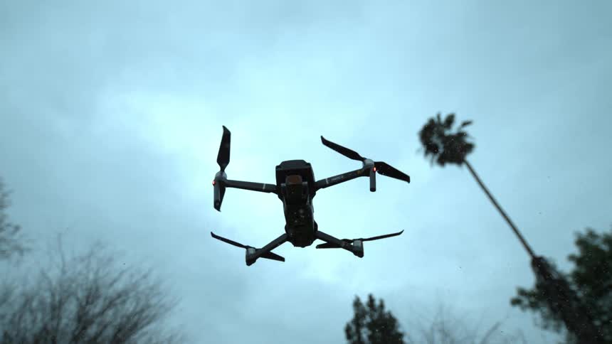 A drone hovers in the air still while the propellers spin