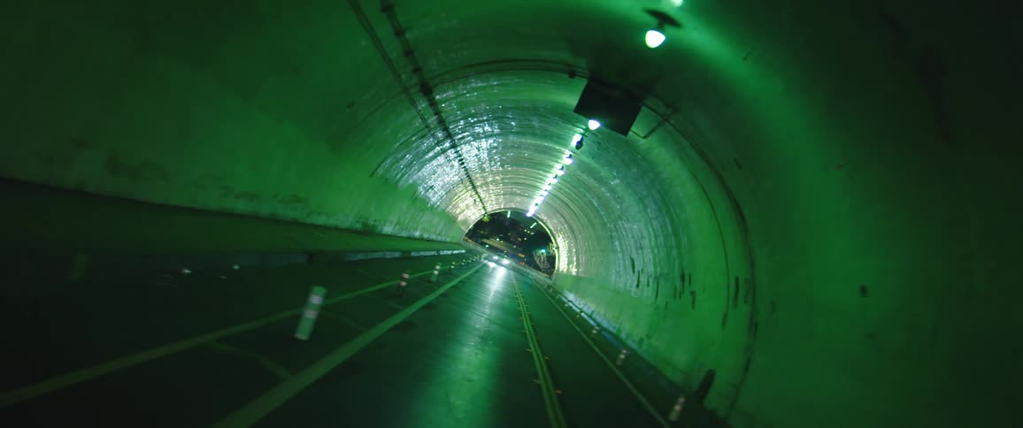 Vehicles travel a dark tunnel towards city lights