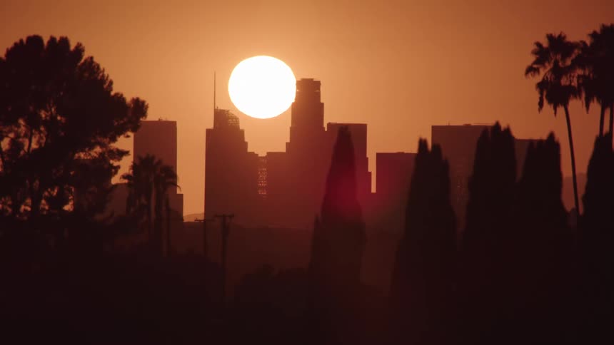 The sun sets behind skyscrapers