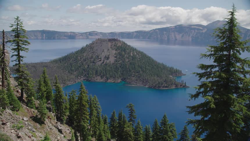 Tree covered island sits in the calm blue lake under a cloudy sky