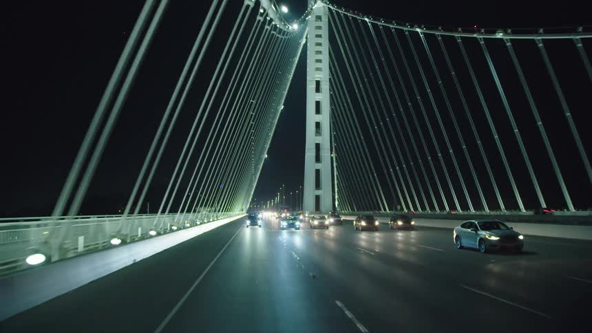Suspension bridge cables glow in the night as cars pass along the bridge