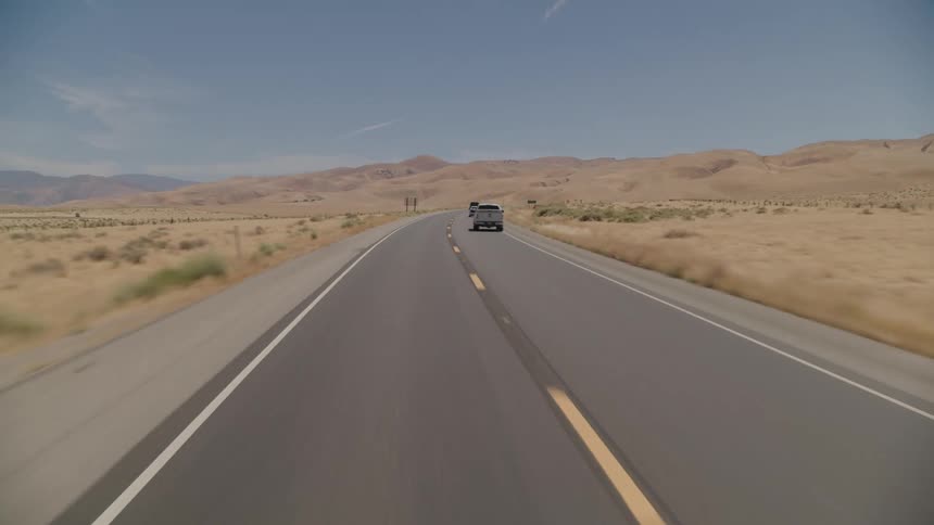 Vehicles travel along road surrounded by plains and mountains