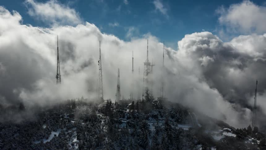 A forest with antennas and a small town engulfed by clouds