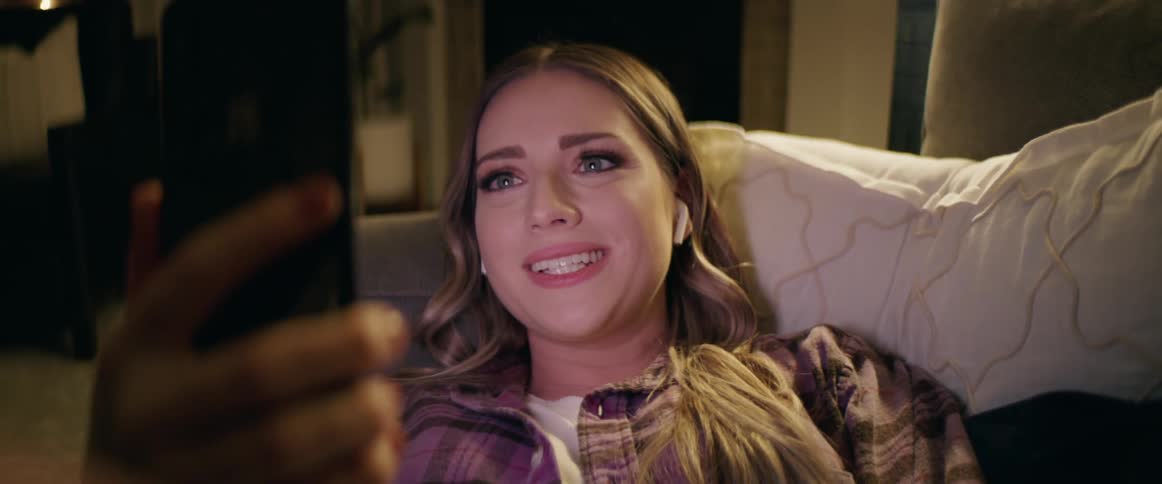 Woman lying down on the sofa makes a video call with a smart phone in the living room