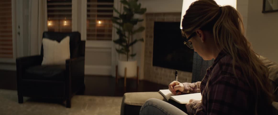 Blonde woman sitting on the couch writes down in the living room