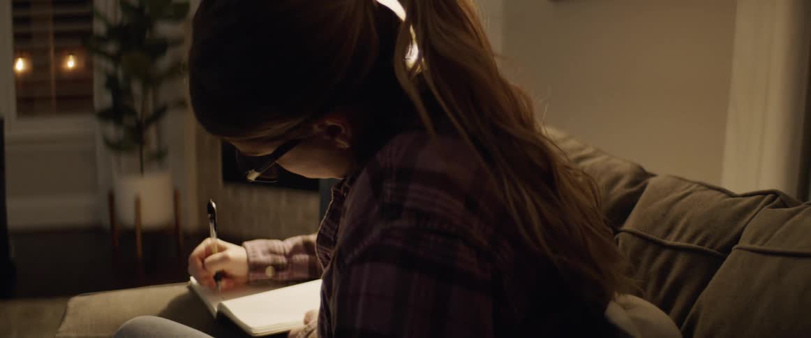 A woman sitting on a couch writing on a notebook