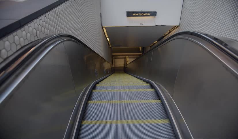 An escalator rides up towards the camera with a sign for montgomery near the ceiling