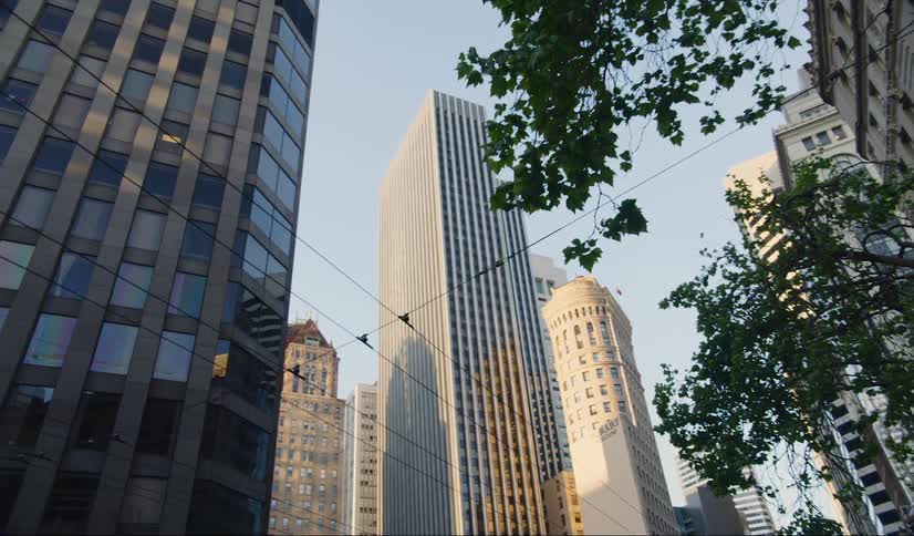 Trolley wire hangs over the city street and trees with skyscrapers standing tall behind