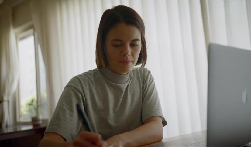 A teenager takes notes as she looks at her laptop