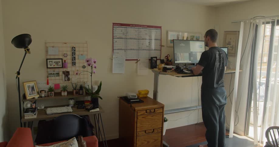 A man works at his home office standing desk near the sliding doors with a breeze