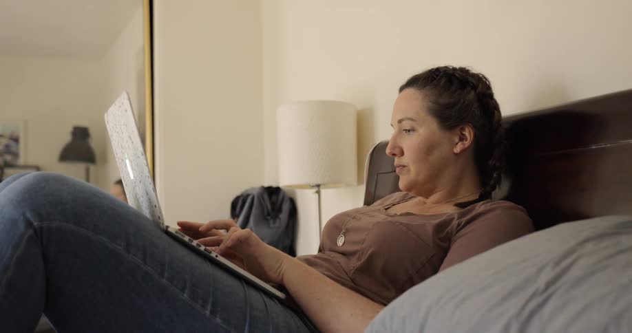 Woman lying down on bed uses a laptop in the bedroom