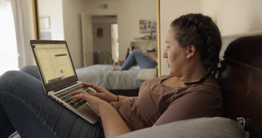 Woman sitting on the bed uses a laptop in the bedroom