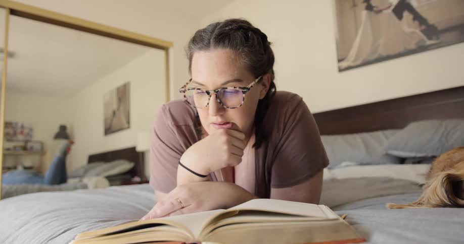 A woman lays on her bed reading a book