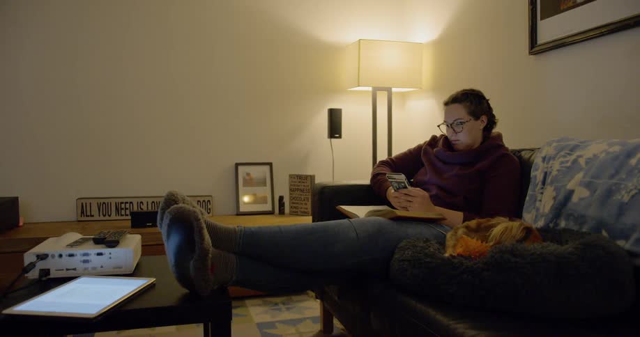 Woman sitting on couch checks phone with pet dog at her side