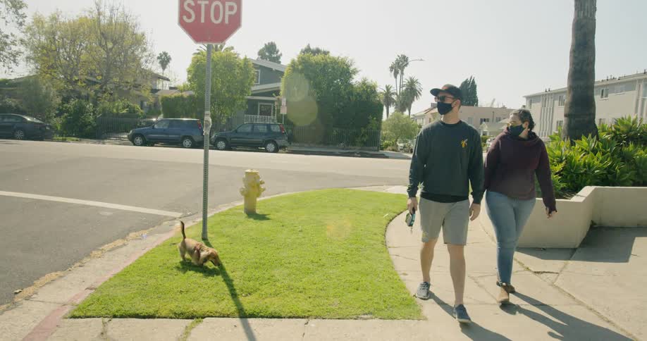 Couple wearing face masks walk dog on neighborhood