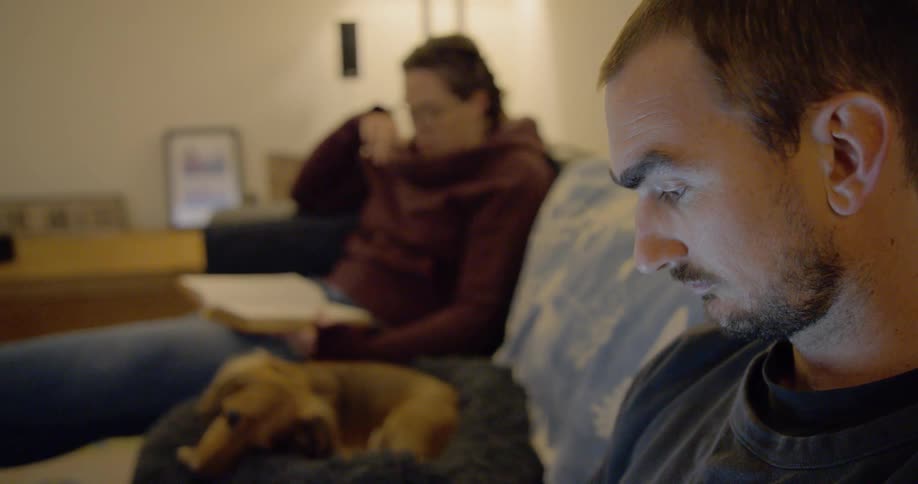 Woman reading a book and man using a smartphone sit on the couch in the living room at home