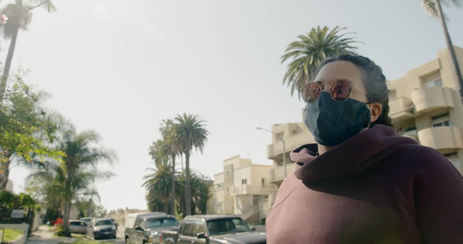 A woman wears a mask while standing on a sidewalk