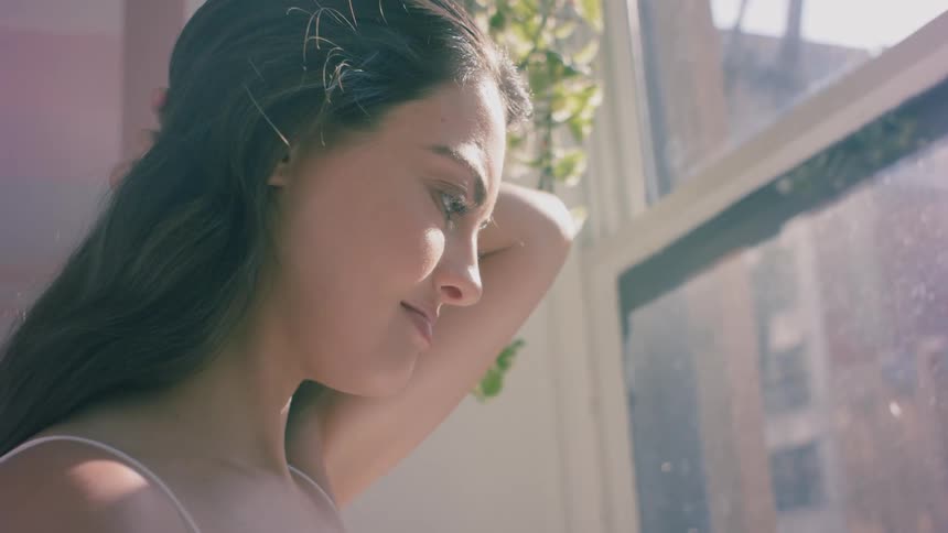 Woman looks out the window of her apartment at day