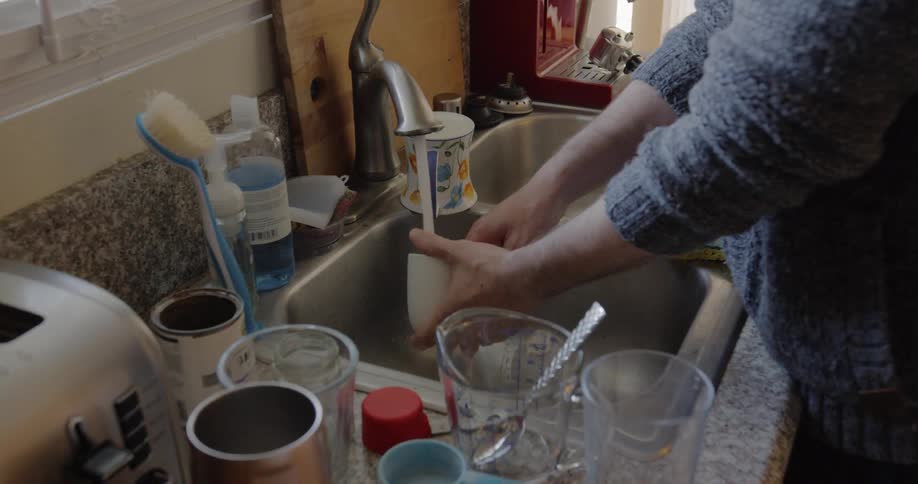 Person washes cup under running faucet in kitchen