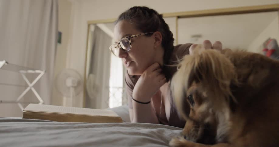 A woman pets a dog while reading