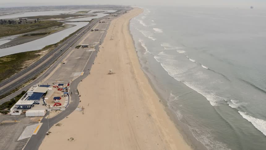 Small waves crash on a mostly empty beach with an adjacent road