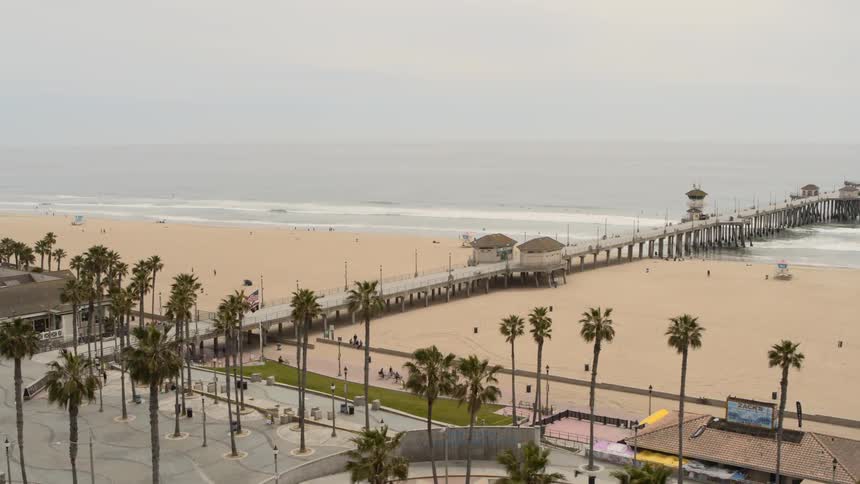 People ride their bikes on the path beside an empty beach and pier