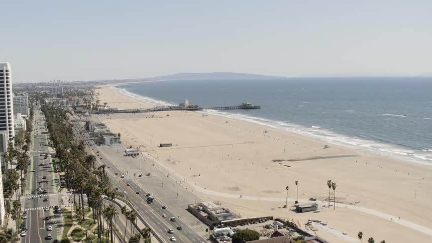Aerial view of the vehicles driving on the city highway next to the golden beach in the city
