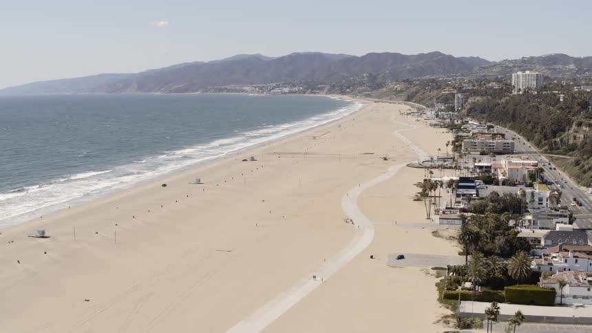 An empty sandy beach with only a few people walking on the path on a sunny day