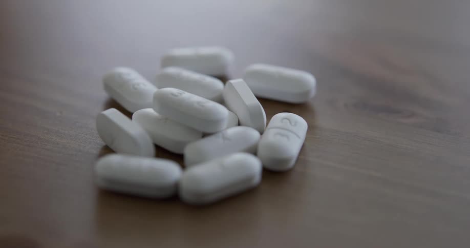 Hand pouring white pills from a plastic medicine bottle onto table