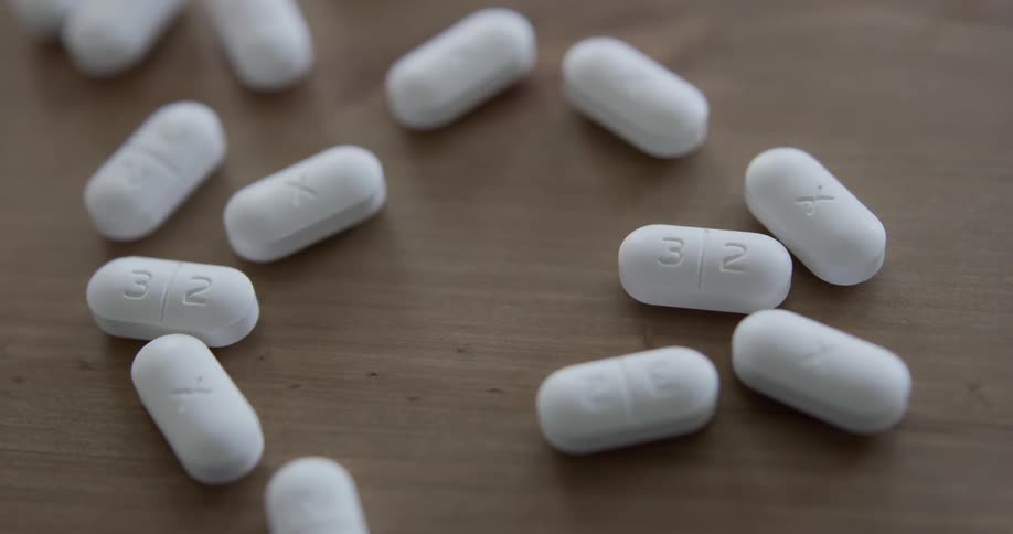 White amoxicillin capsules are spilled out onto a wood grain surface