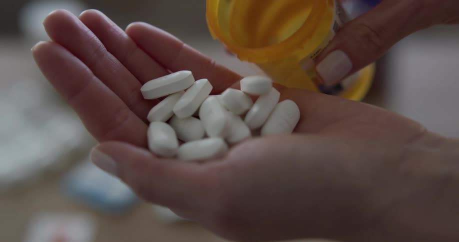 Person pours white medical tablets from medicine container into their palm