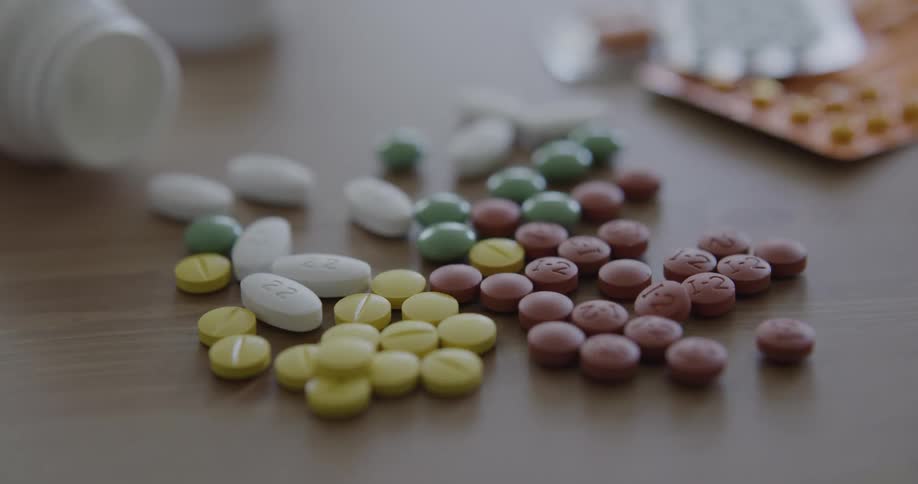 Several different pills and capsules on a table with pill bottles on their sides