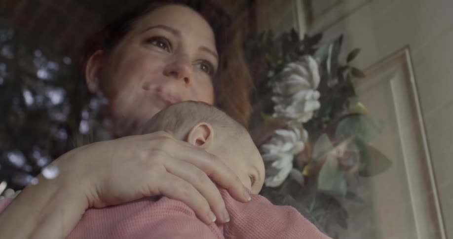 A woman holds an infant standing at a doorway looking outside