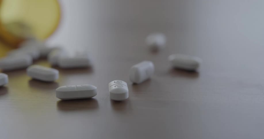 A pill bottle falls and spills white capsules