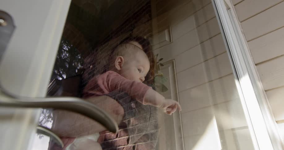 A woman holds a baby inside a home by the front door looking out