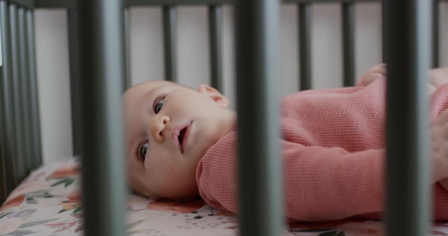 Baby lies on back in crib looking around