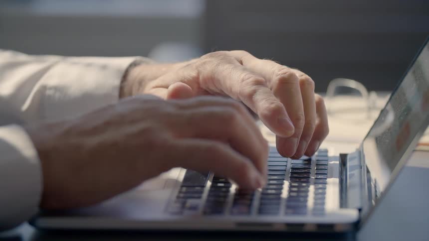 A doctor types on a laptop sitting on a desk