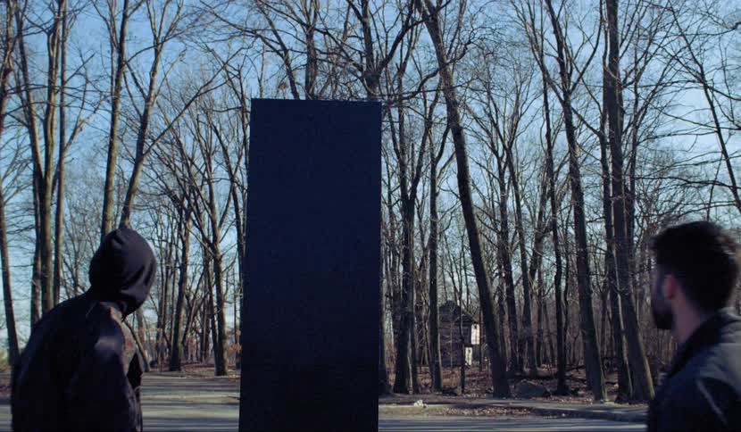 A group of dancers stands and looks at the stele in the woods