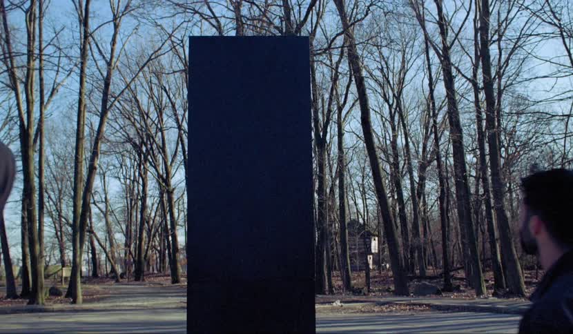 A group of teens stand outside facing a big black board