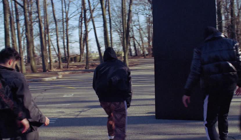 Men in a park dancing around a black pillar