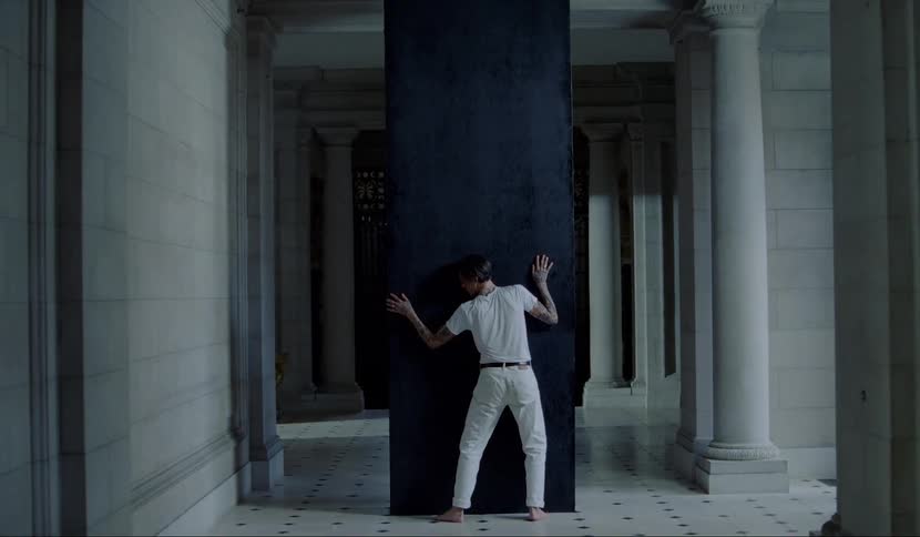 A man pressing his body against a large black monolith in a hallway