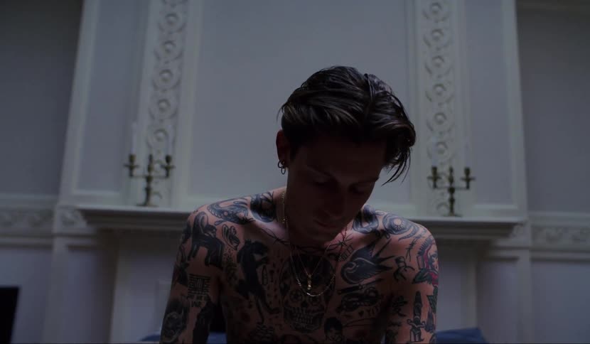 Shirtless tattooed young man sitting in bed on luxurious room