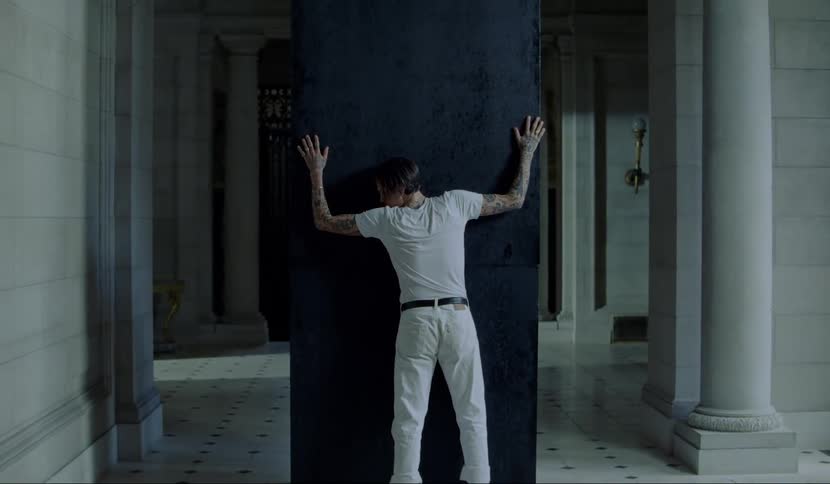 A man touches and then hugs a tall black box in the middle of a hallway