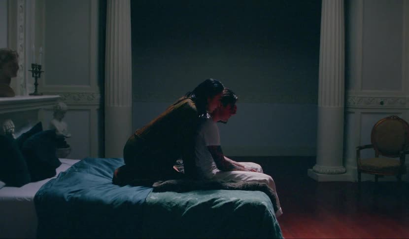 A woman leans over a mans shoulder in bed