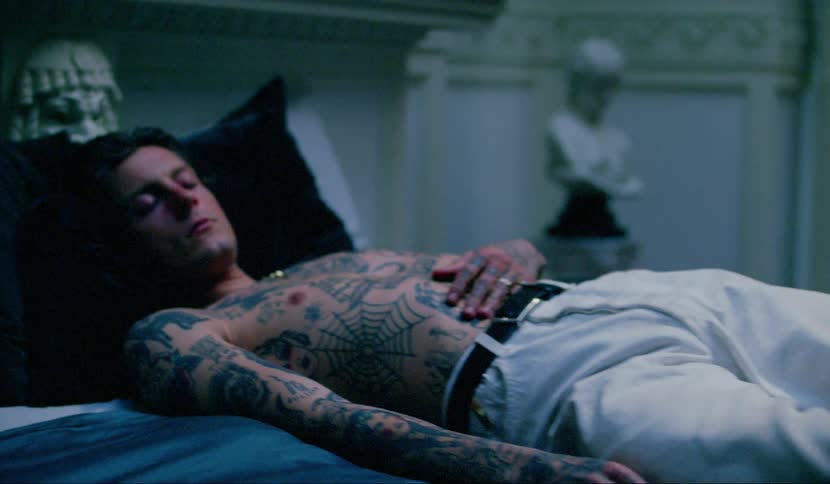 A male teenager covered in tattoos lies on a bed sleeping