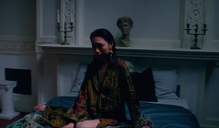 An asian woman sits on a bed in a spacious bedroom with large columns