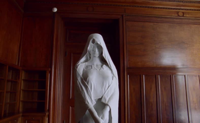 White of statue of woman in shawl stands out against wood paneling and furnishing of room