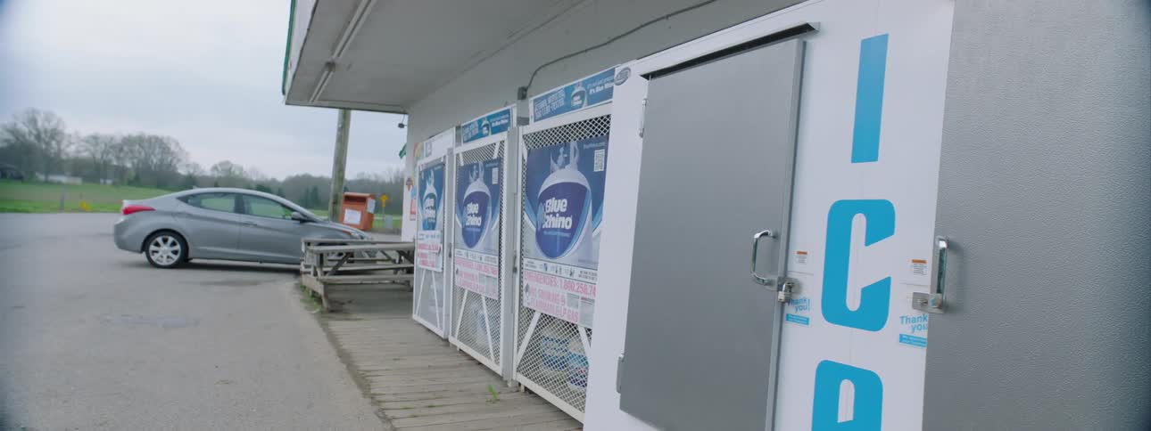 A vehicle is parked outside of a convenient store with ice bins and propane tanks