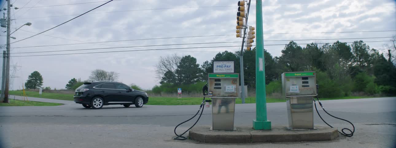 Vehicles driving by vintage gas pumps in a small town